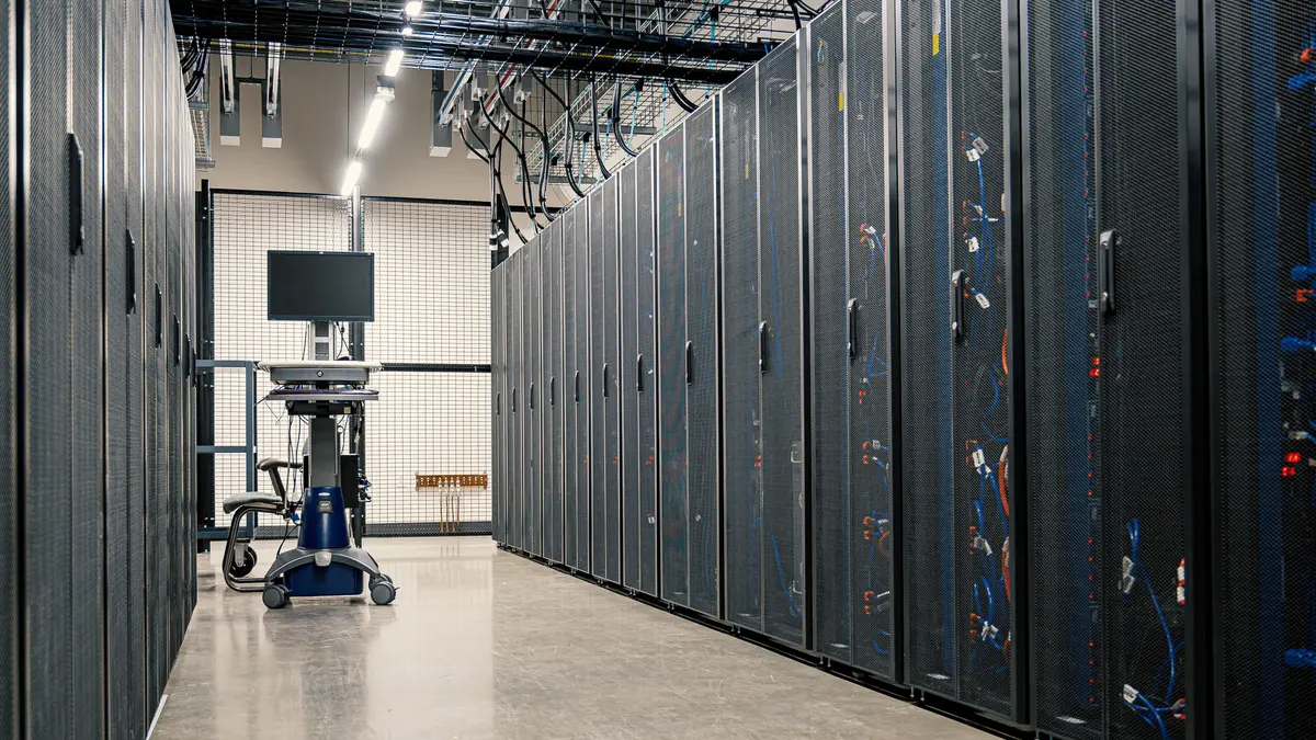 Corredor de data center com racks de servidores, cabos e equipamentos de rede