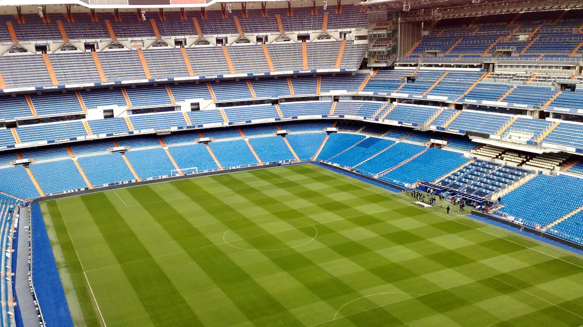 Vista aérea de estádio de futebol com gramado verde e arquibancadas azuis
