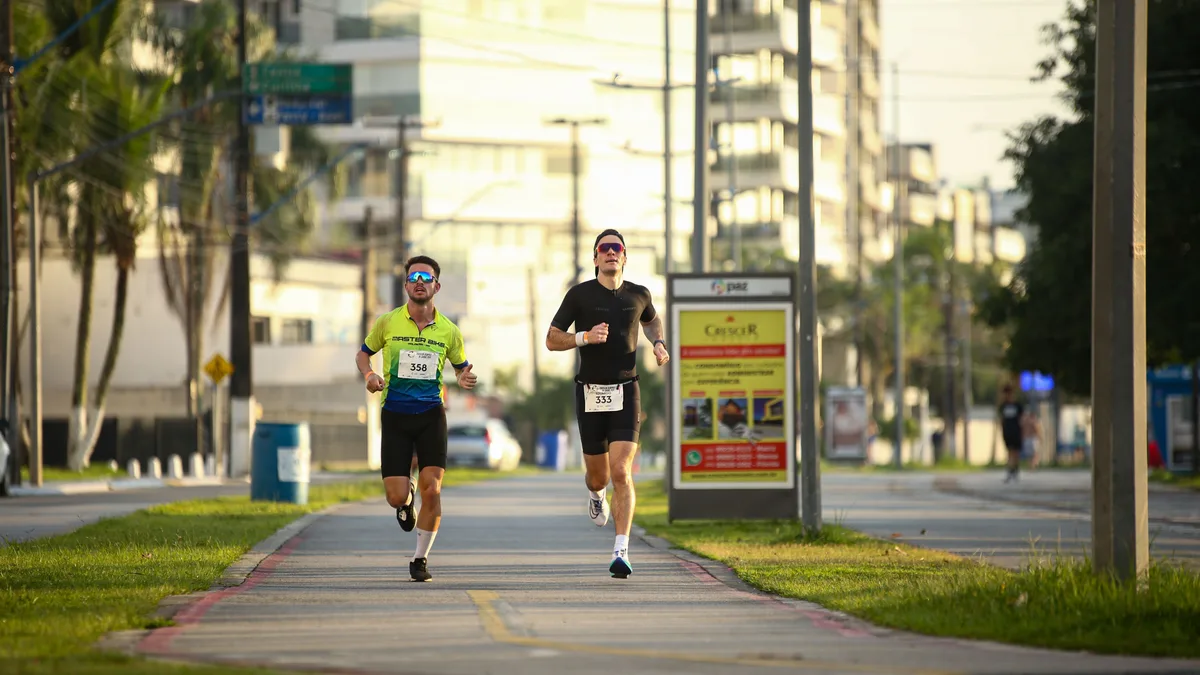 Dois homens correndo lado a lado em uma via urbana durante o dia