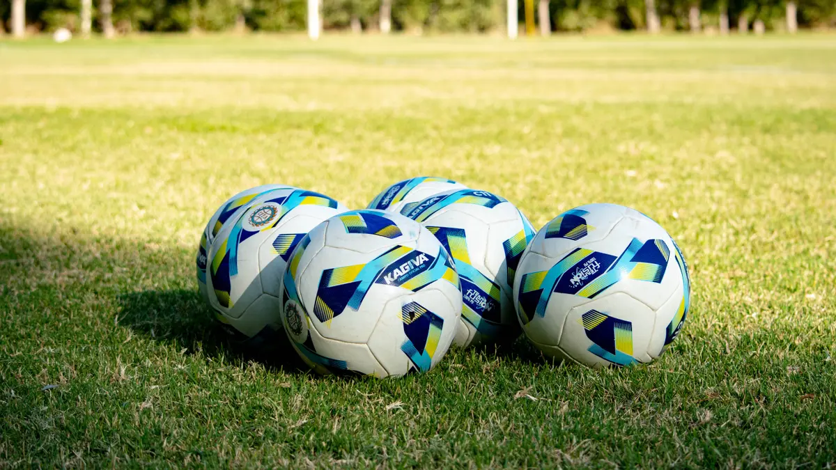 Bolas de futebol enfileiradas sobre gramado verde diante de um gol