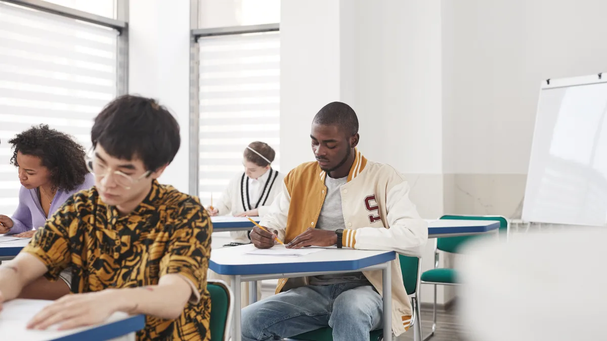 Estudantes concentrados fazendo prova em carteiras de sala de aula