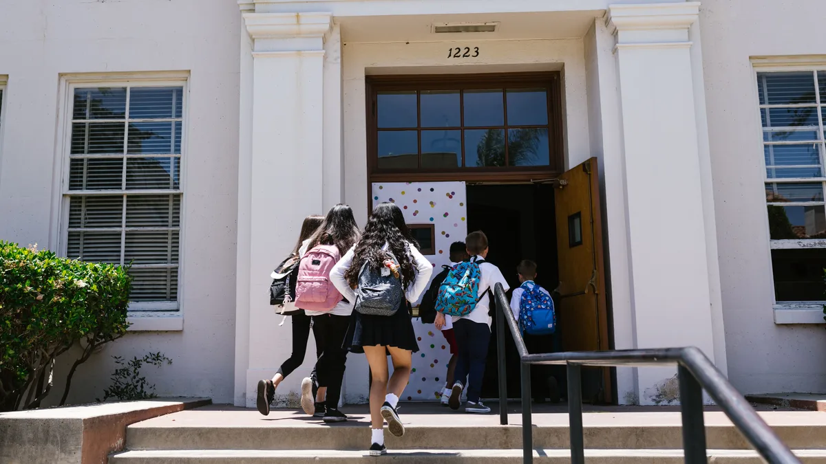 Estudantes de mochila entrando juntos em um prédio escolar