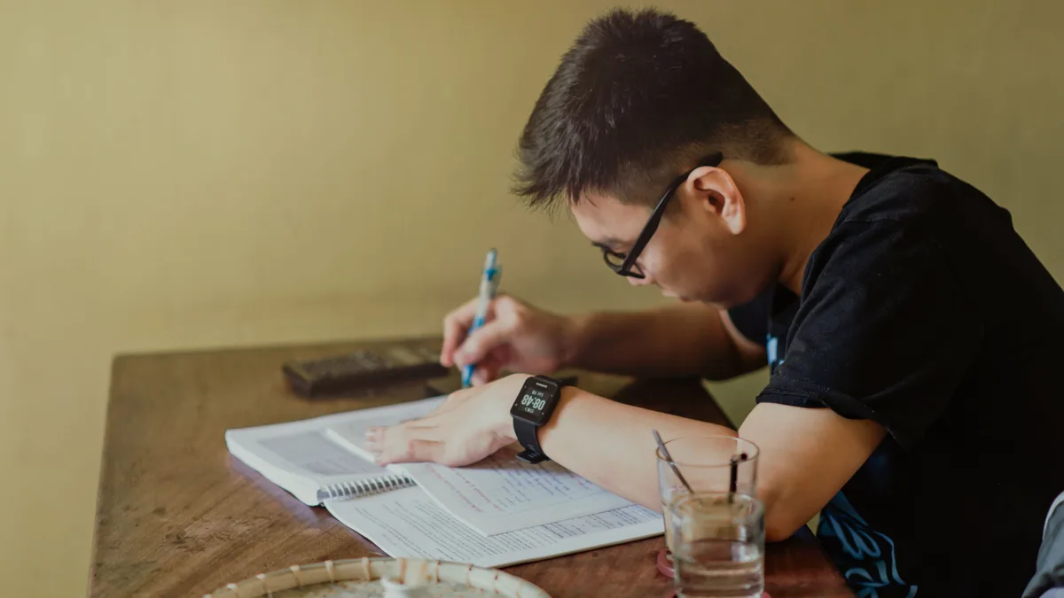Jovem estudando à mesa, fazendo anotações em um caderno