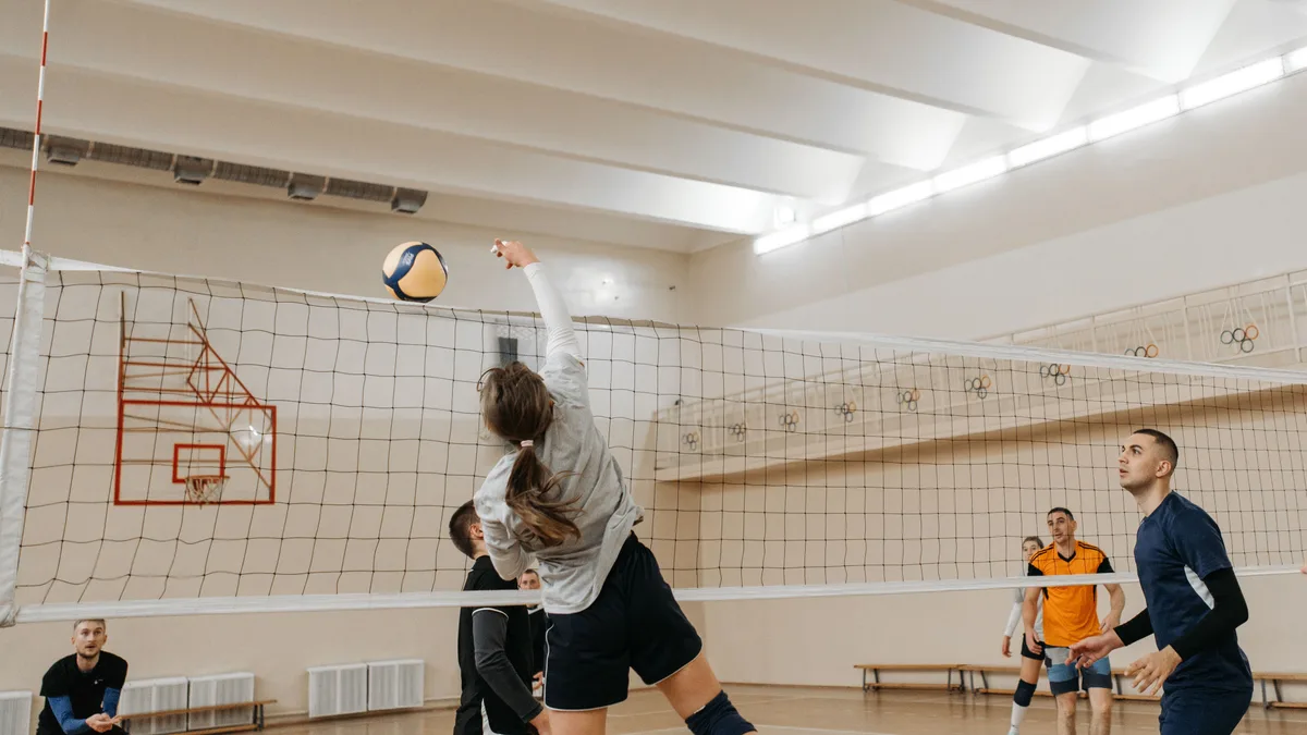 Jogadoras disputam ponto junto à rede em partida de vôlei em quadra coberta