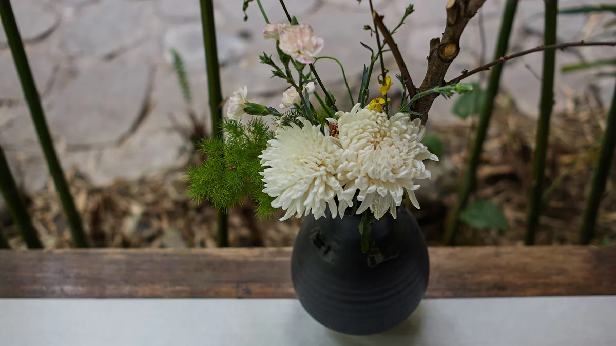 Arranjo floral de crisântemos brancos em vaso de cerâmica preta sobre mesa rústica