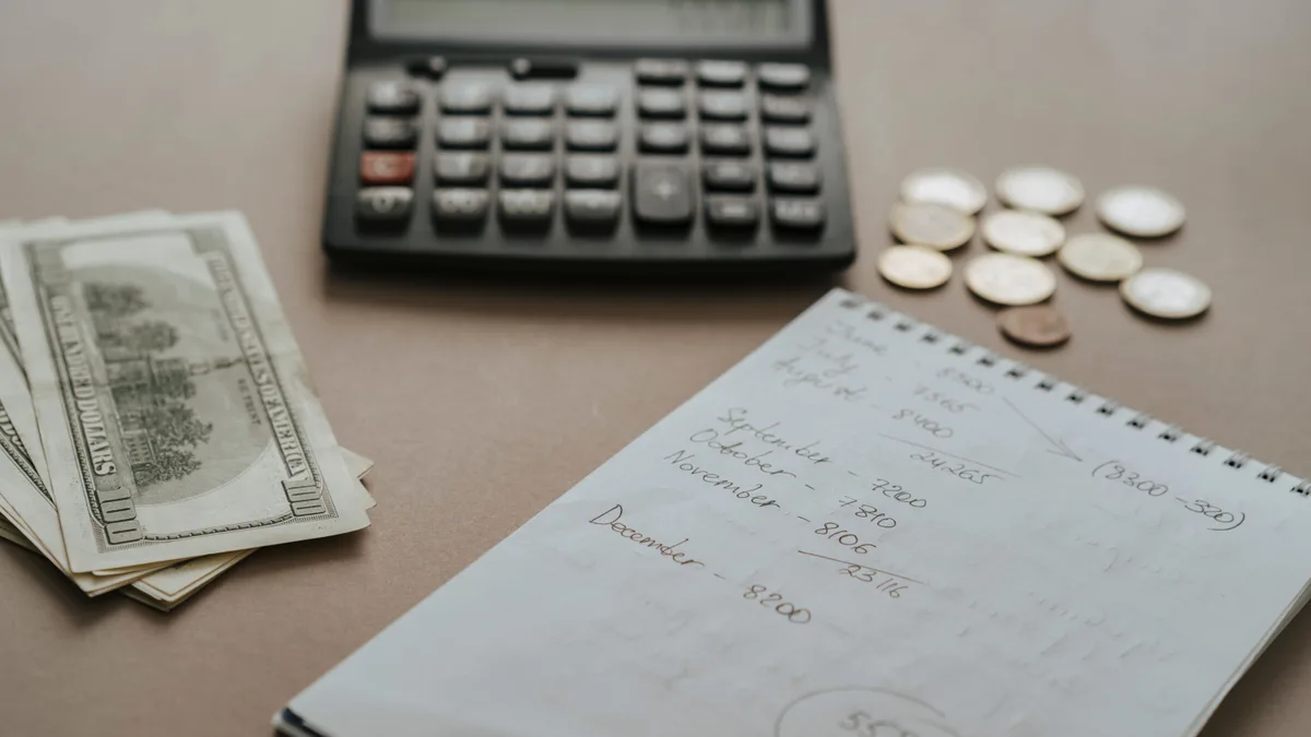 Mesa com calculadora, cédulas, moedas e anotações de orçamento