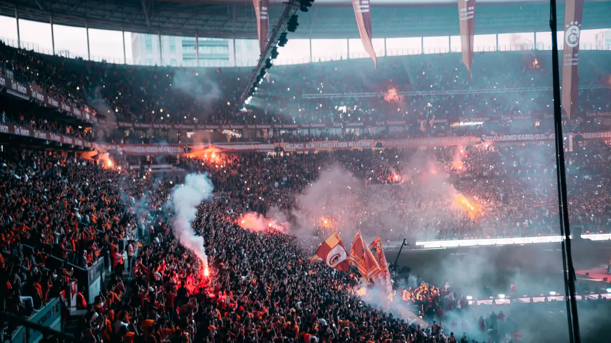 Torcida com sinalizadores acesos lota a arquibancada de um estádio de futebol