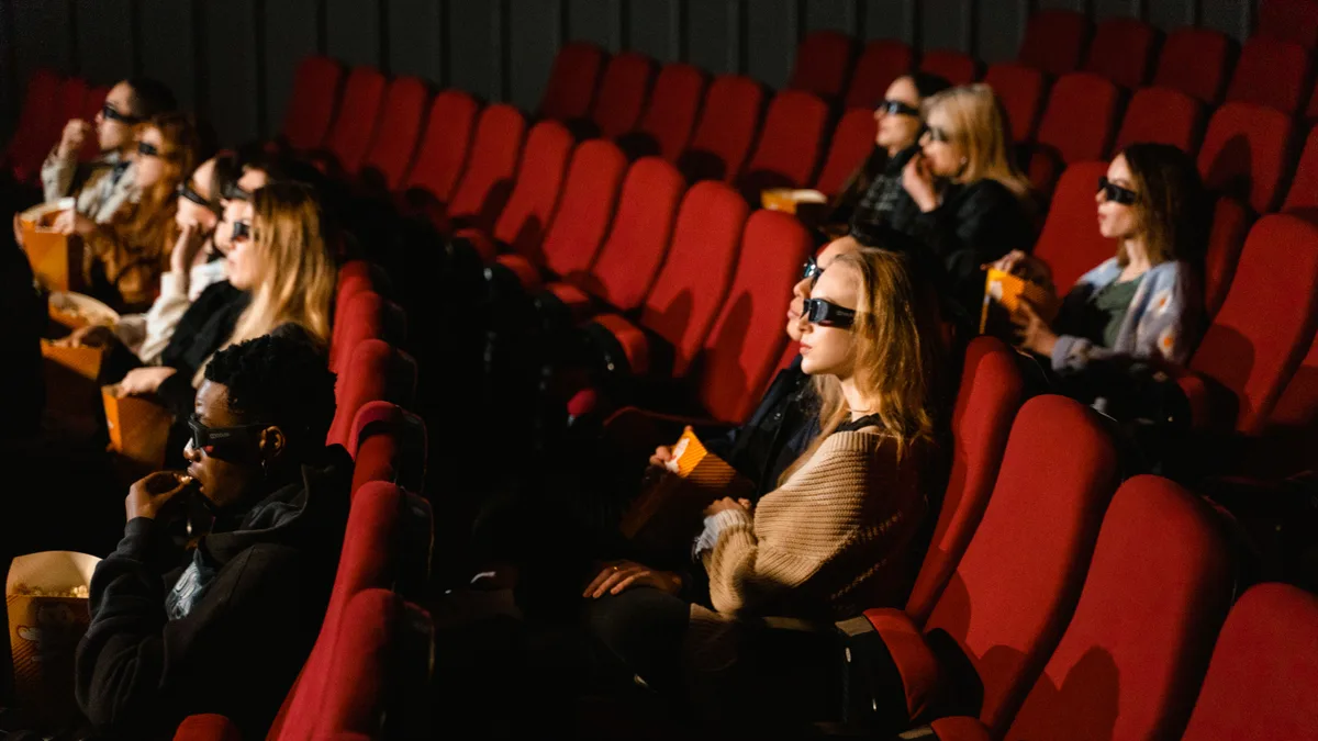 Plateia de cinema com óculos 3D comendo pipoca em sala de poltronas vermelhas