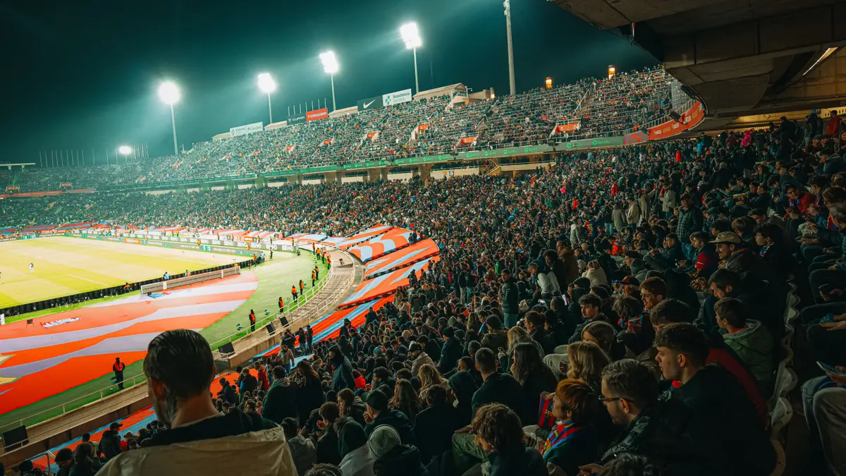 Jogo de futebol à noite, com o estádio cheio de torcedores nas arquibancadas