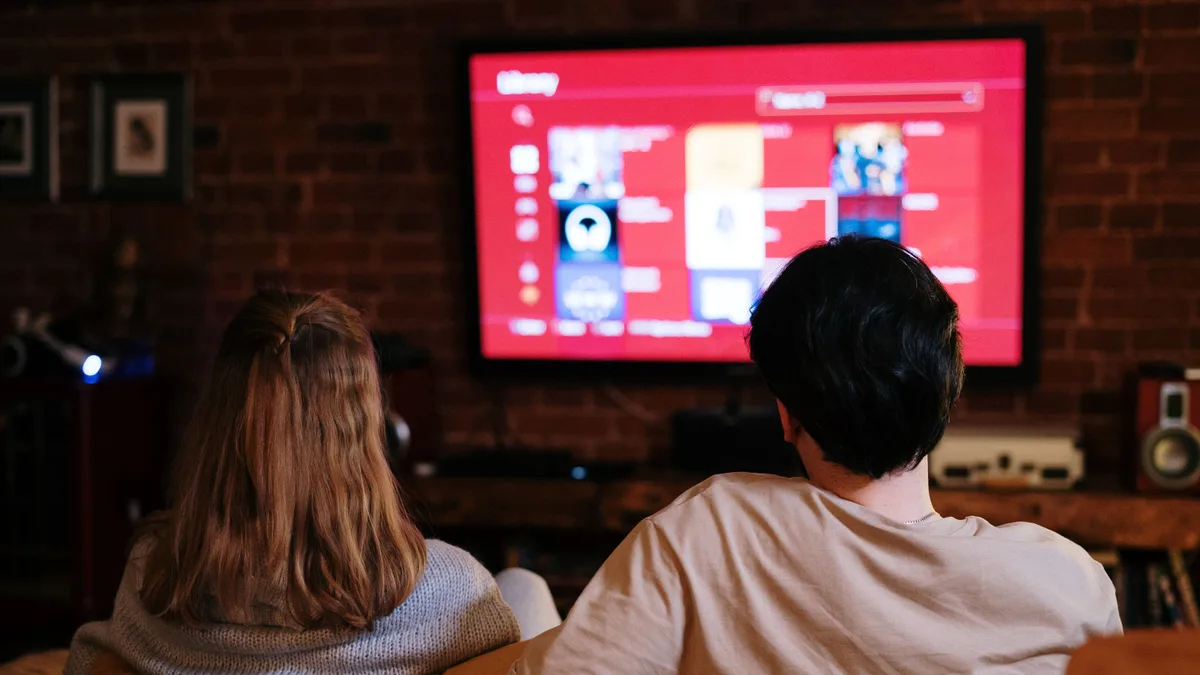 Casal assiste a streaming em uma TV grande, em sala aconchegante de parede de tijolos
