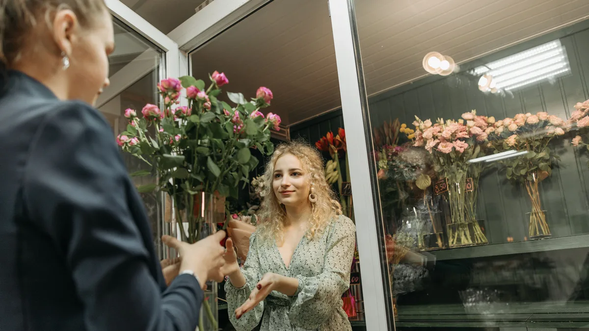 Florista entrega um buquê de flores a uma cliente no balcão de uma floricultura