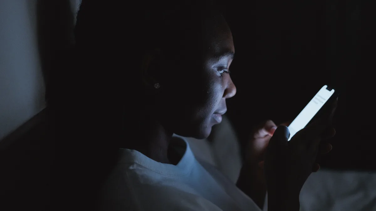 Mulher relendo mensagens no celular em quarto escuro, iluminada pela tela