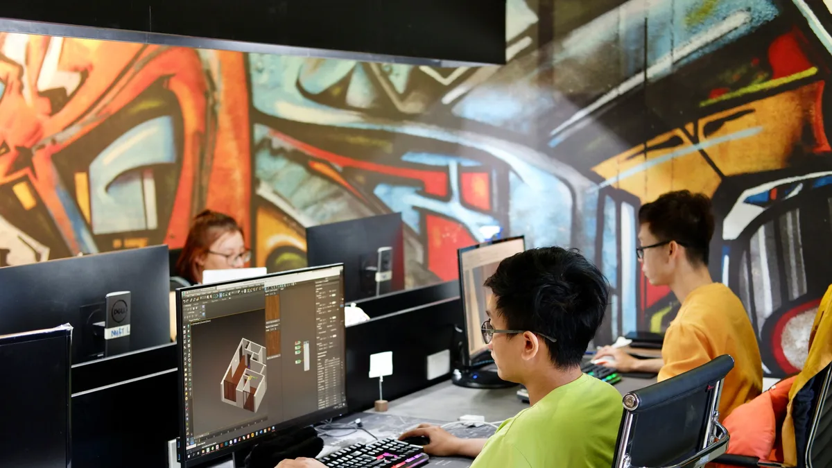 Três jovens trabalham em computadores em um escritório descontraído, com parede grafitada