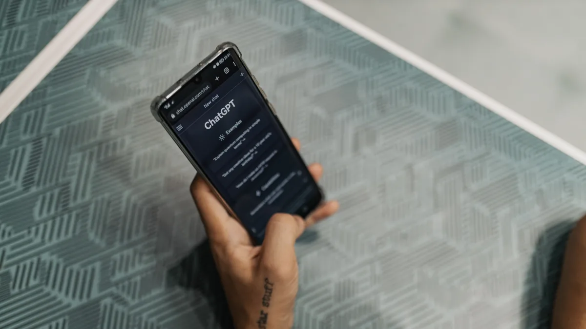 Mão segura um smartphone com o aplicativo do ChatGPT aberto sobre uma mesa