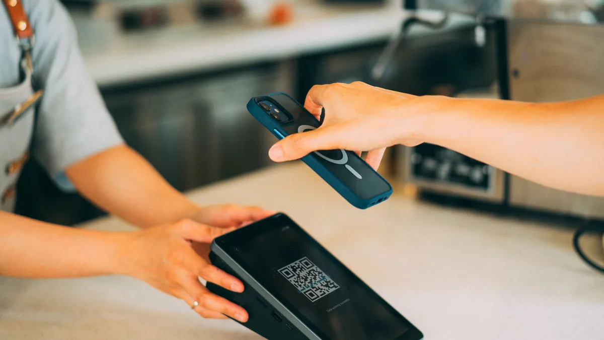 Pessoa aproxima o celular de uma maquininha com QR code para pagar em uma loja