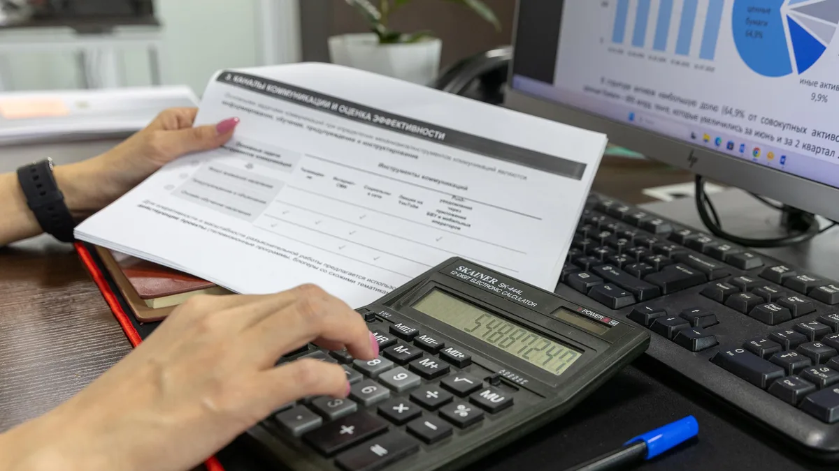 Mãos usando uma calculadora sobre documentos financeiros em uma mesa de escritório
