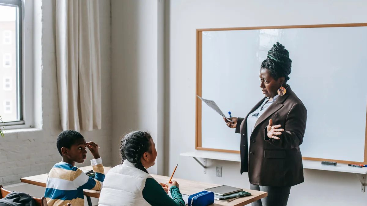 Professora explicando conteúdo no quadro branco para alunos em sala de aula