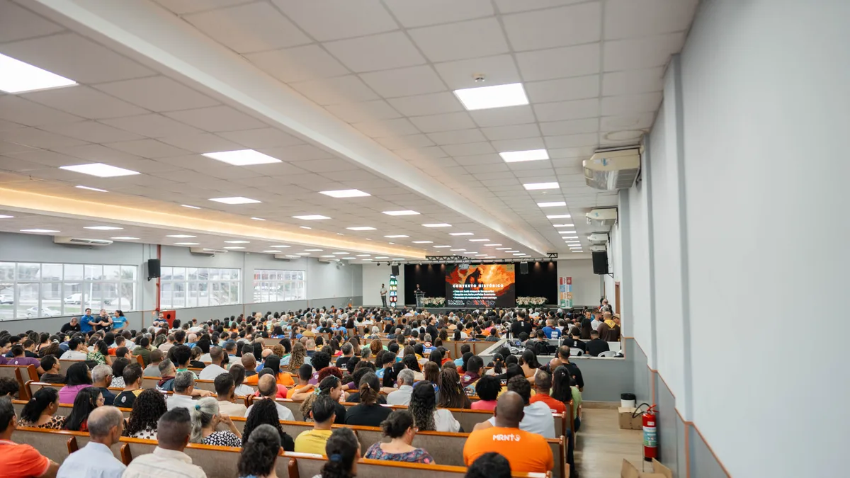 Auditório lotado durante um grande evento, com plateia voltada para o palco iluminado
