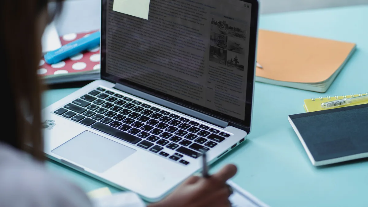 Grupo de estudantes reunidos com notebook, estudando e escrevendo em papel