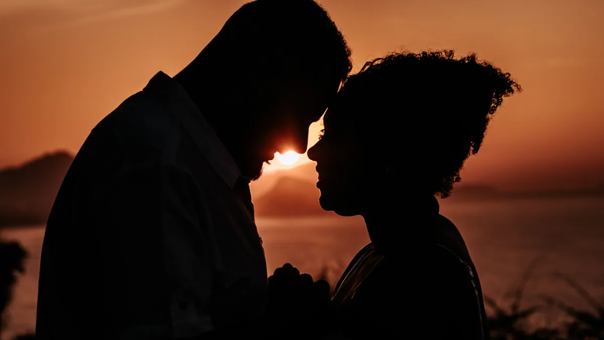 Casal em silhueta compartilha momento íntimo diante do céu do entardecer